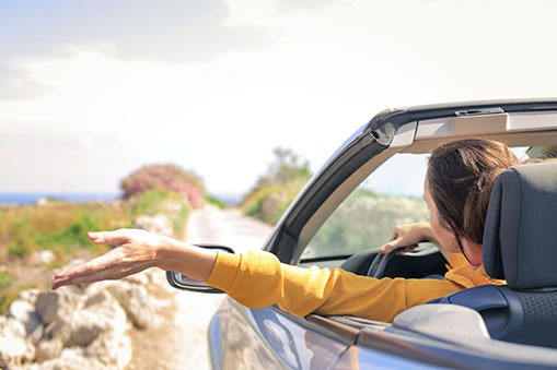 a woman driving to the beach as her hand is outside the car